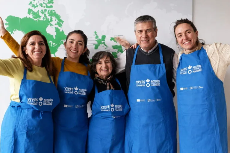 Cinco personas con delantal azul de Vives Emplea sonríen delante de un mapa del mundo